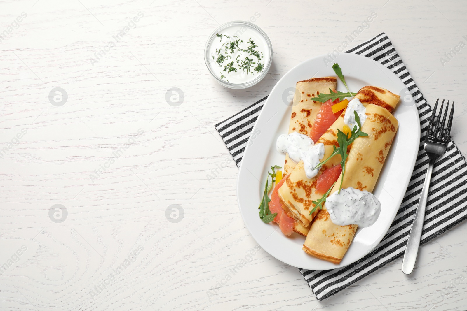 Photo of Delicious thin pancakes with salmon and sour cream on white wooden table, flat lay. Space for text