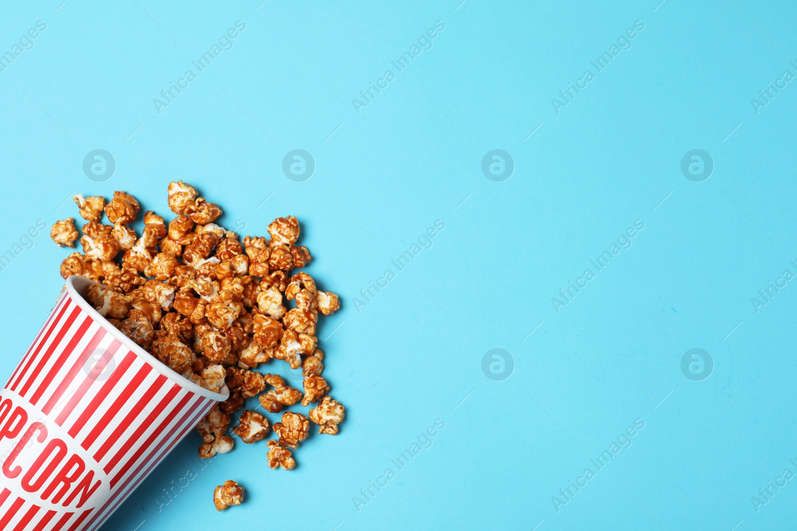 Photo of Overturned paper cup with caramel popcorn on color background, top view. Space for text