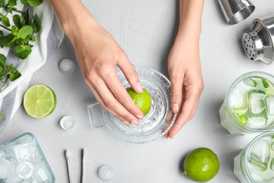 Photo of Woman making fresh lime juice for Mojito cocktail at light table, top view