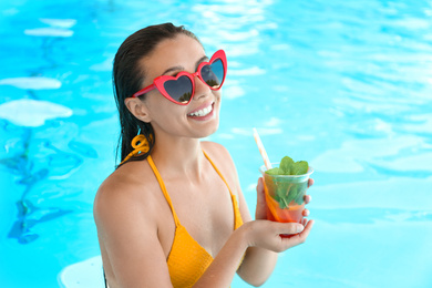 Woman with glass of refreshing drink in swimming pool