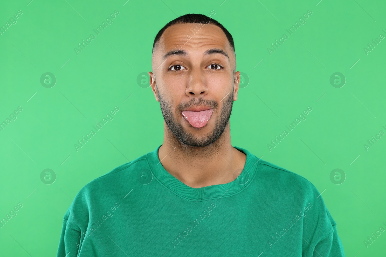 Photo of Young man showing his tongue on green background