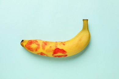 Photo of Banana with red lipstick marks on turquoise background, top view. Sex concept