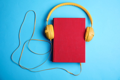Book and modern headphones on light blue background, top view