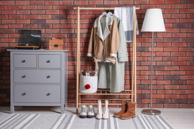 Photo of Beautiful hallway interior with coat rack and chest of drawers near red brick wall