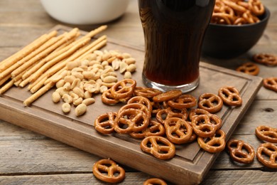 Photo of Glass of beer served with delicious pretzel crackers and other snacks on wooden table, closeup