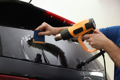 Worker tinting car window with heat gun in workshop, closeup