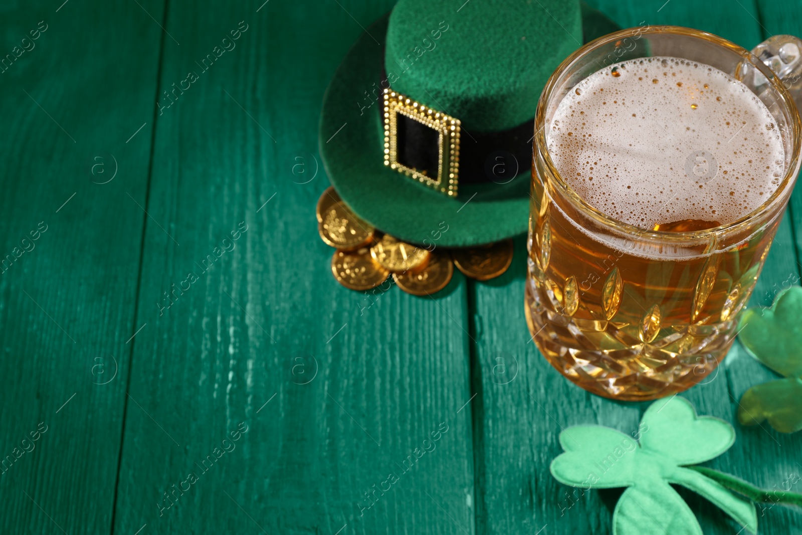 Image of St. Patrick's day. Beer, leprechaun hat, gold and decorative clover leaves on green wooden table. Space for text