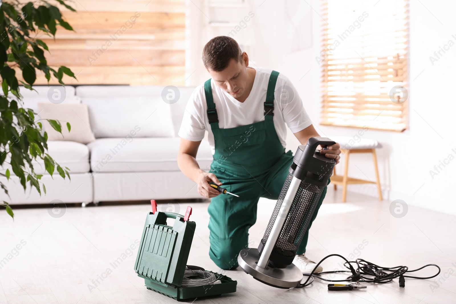 Photo of Professional technician repairing electric patio heater with screwdriver indoors