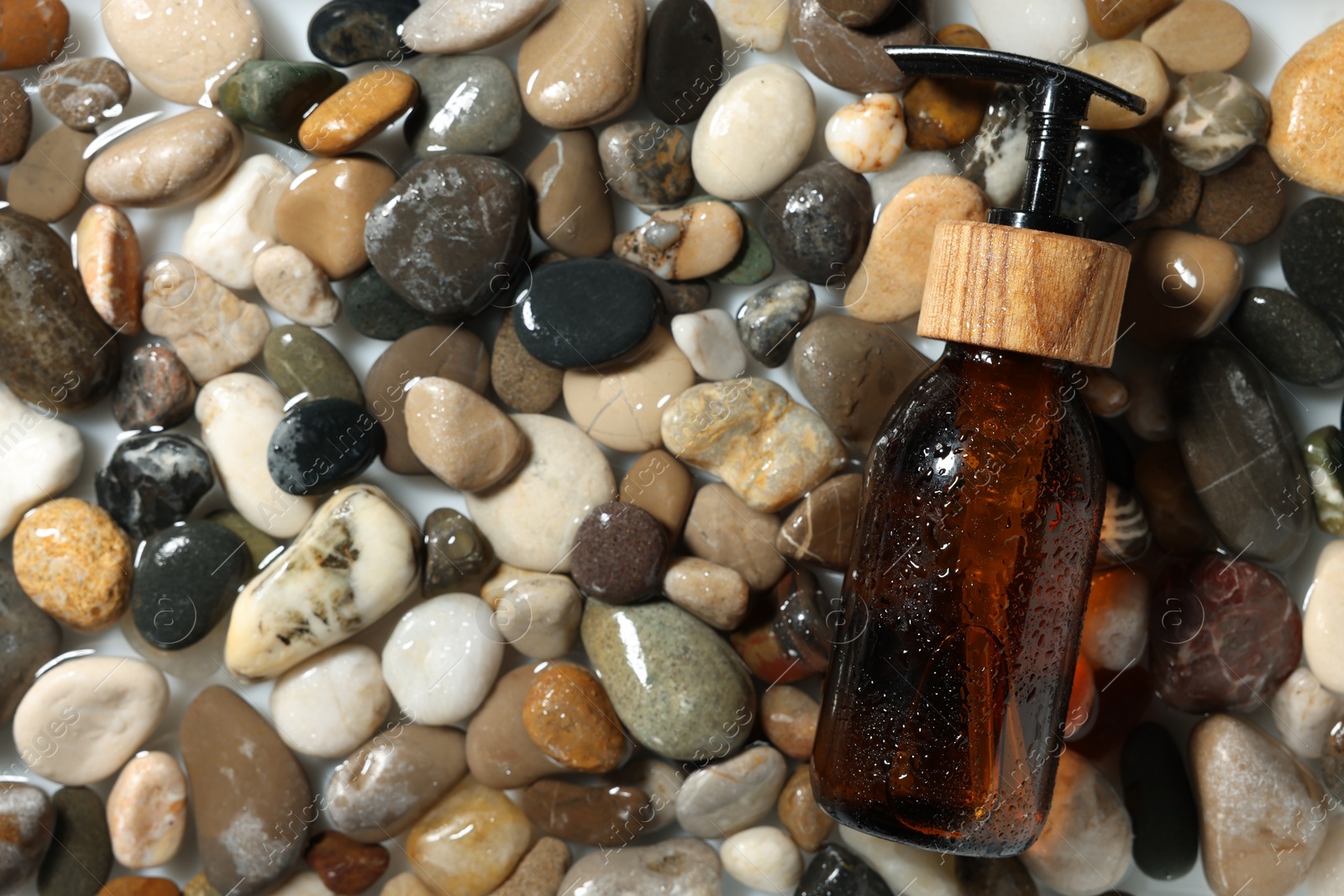 Photo of Bottle of cosmetic product on wet stones, top view. Space for text