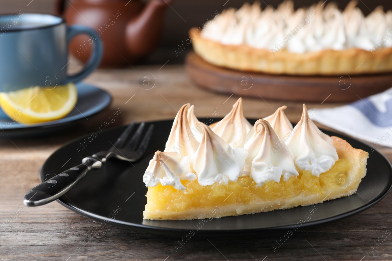 Photo of Piece of delicious lemon meringue pie served on wooden table, closeup