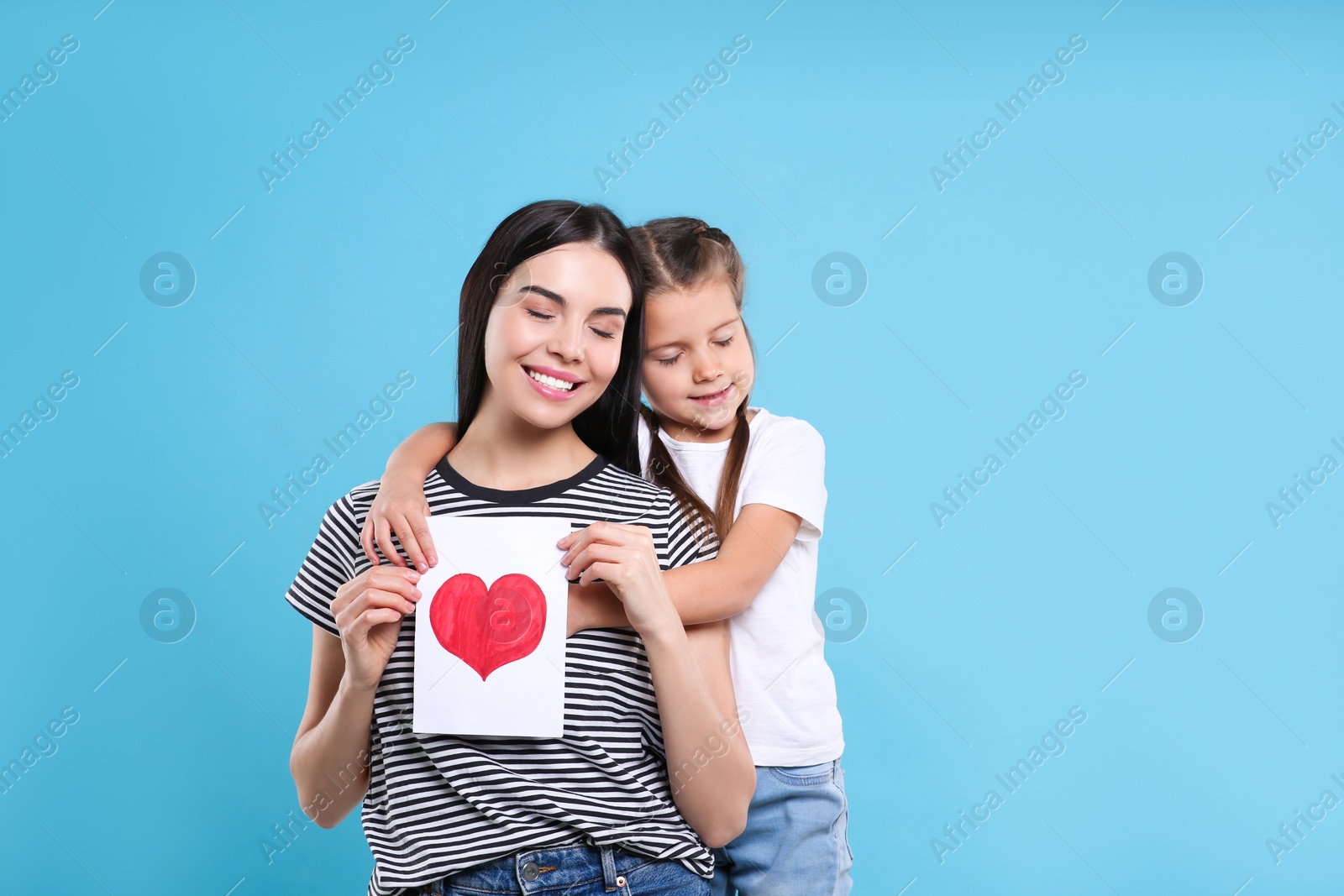 Photo of Happy woman with her cute daughter and handmade greeting card on light blue background, space for text. Mother's day celebration