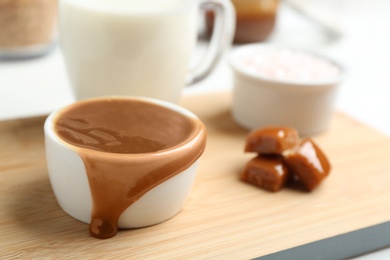 Photo of Bowl with caramel sauce and candies on board, closeup