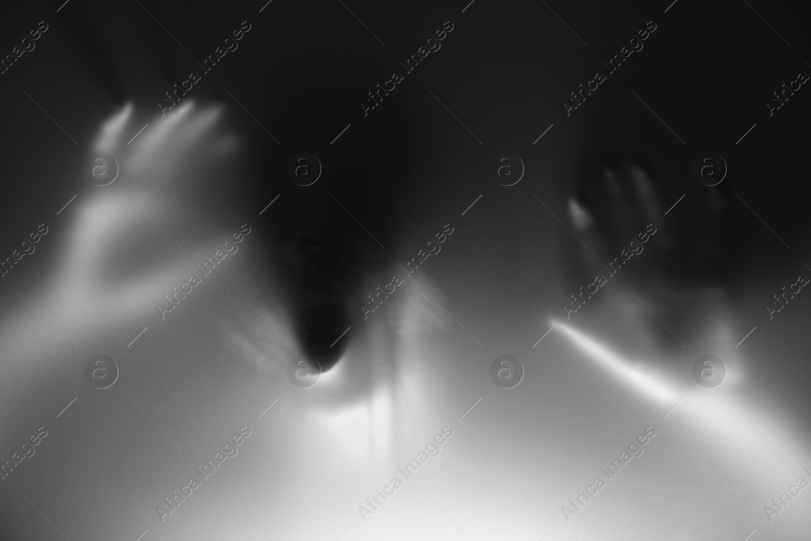 Photo of Silhouette of creepy ghost behind glass against grey background