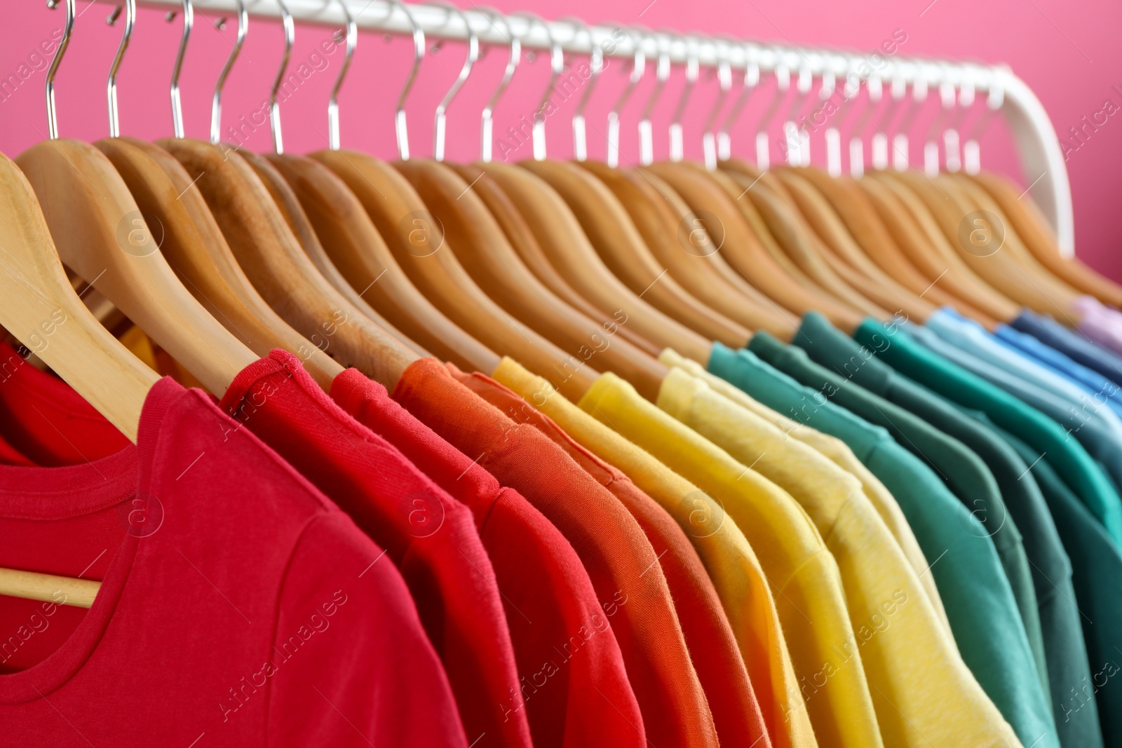 Photo of Rack with bright clothes on pink background. Rainbow colors