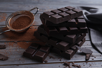 Photo of Tasty dark chocolate bars and sieve with cocoa powder on wooden table