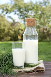 Photo of Tasty fresh milk and green grass on wooden table