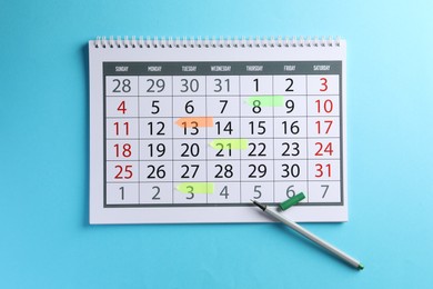 Photo of Timetable. Calendar with marked dates and pen on light blue background, top view