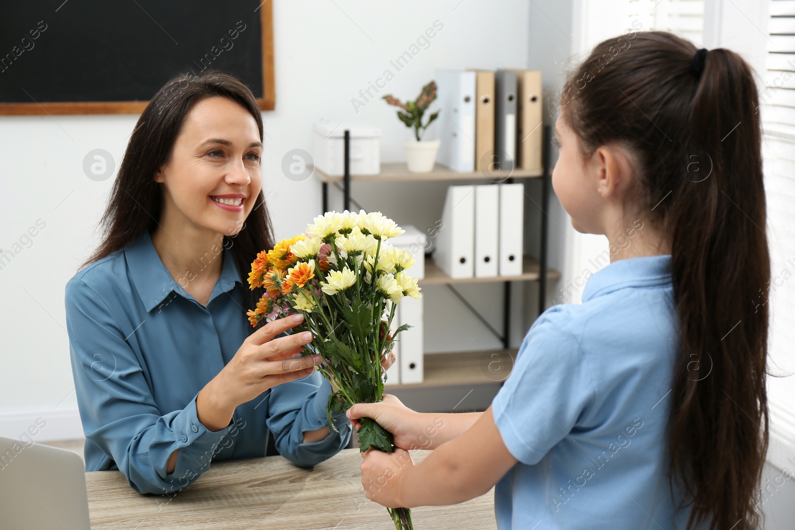 Photo of Schoolgirl congratulating her pedagogue with bouquet in classroom. Teacher's day