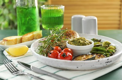 Photo of Tasty chicken, vegetables with tarragon and pesto sauce served on green wooden table