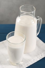 Carafe and glass of fresh milk on blue wooden table, closeup