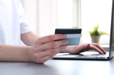 Photo of Online payment. Woman with laptop and credit card at white table, closeup