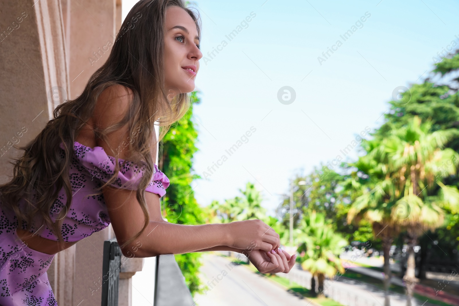 Photo of Beautiful young woman standing on balcony, space for text