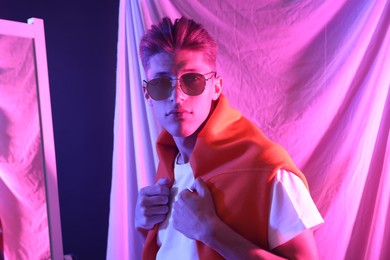 Photo of Stylish young man with sunglasses indoors in neon lights