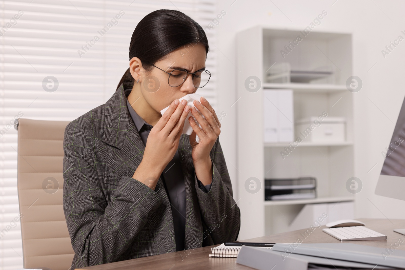 Photo of Woman with tissue coughing at table in office. Cold symptoms