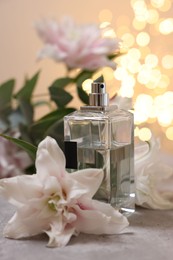 Bottle of perfume and beautiful lily flowers on table against beige background with blurred lights, closeup