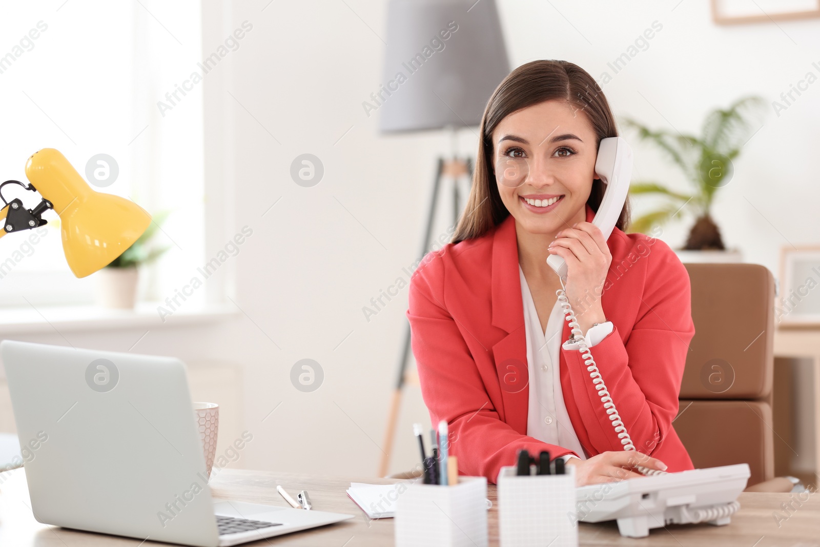 Photo of Young woman talking on phone at workplace