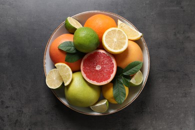 Photo of Different fresh citrus fruits and leaves on grey textured table, top view