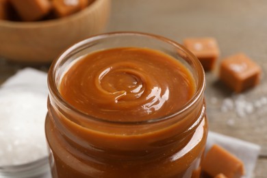 Yummy salted caramel in glass jar on table, closeup