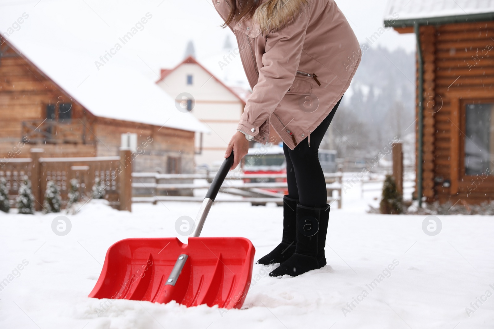 Photo of Young woman cleaning snow with shovel near her house