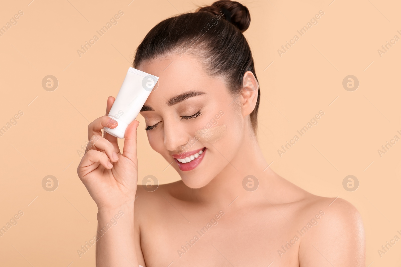 Photo of Woman holding tube of foundation on beige background