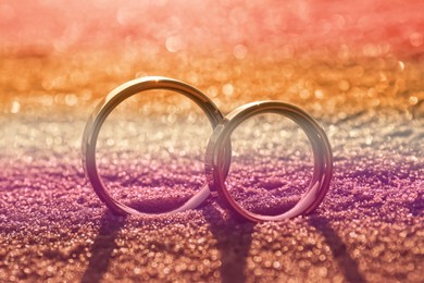 Image of Double exposure of lesbian flag and wedding rings on sandy beach, closeup