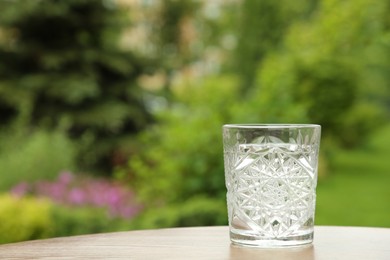 Photo of Glass of fresh water on wooden table outdoors, space for text