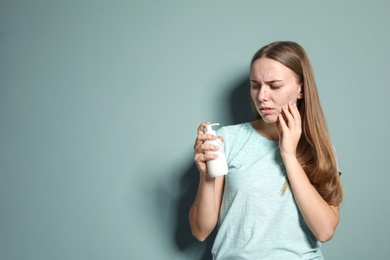 Young woman with acne problem holding bottle with cosmetic product on color background