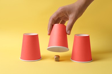 Photo of Woman showing dice under cup on yellow background, closeup. Thimblerig game