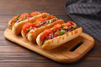 Tasty hot dogs with green onion, tomato, pickles and sauce on wooden table, closeup