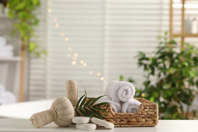 Photo of Spa composition. Herbal bags, towels, stones and palm leaves on white table indoors, space for text