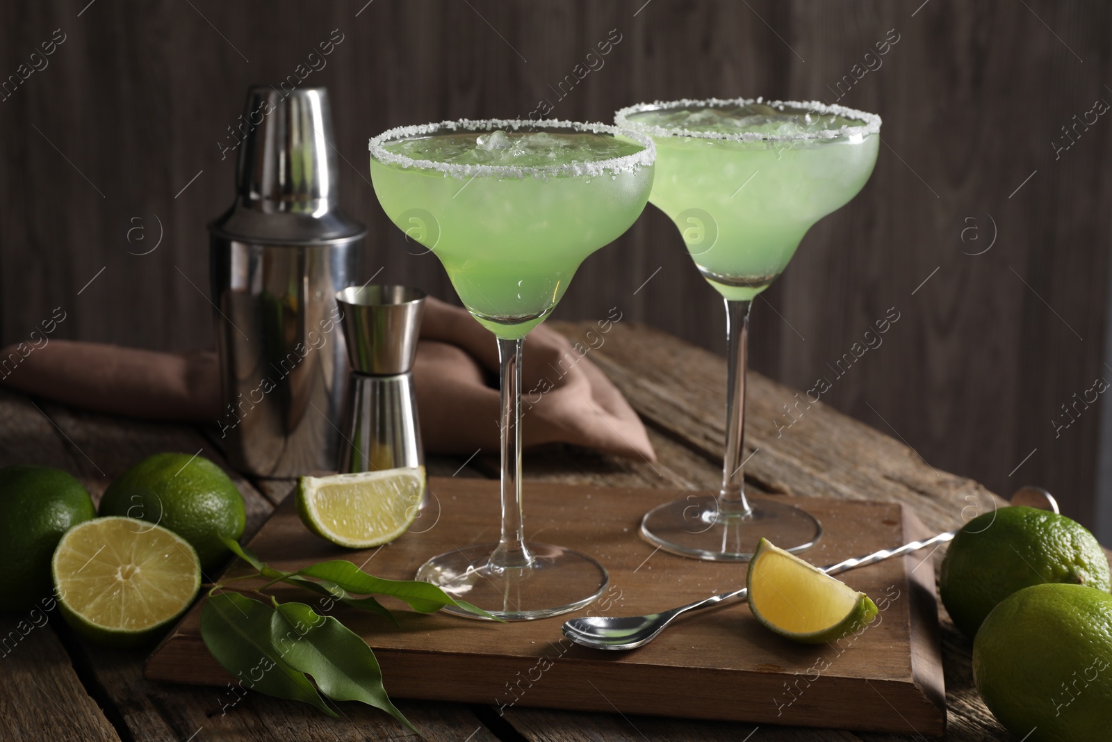 Photo of Delicious Margarita cocktail in glasses, limes and bartender equipment on wooden table