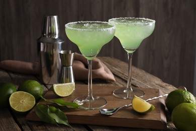 Photo of Delicious Margarita cocktail in glasses, limes and bartender equipment on wooden table