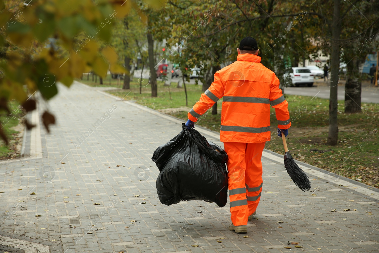 Photo of Street cleaner with broom and garbage bag outdoors on autumn day, back view