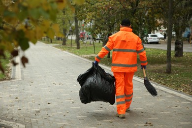 Street cleaner with broom and garbage bag outdoors on autumn day, back view