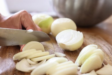 Photo of Woman cutting fresh ripe onion on wooden board, closeup