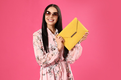 Photo of Young woman wearing floral print dress with elegant clutch on pink background