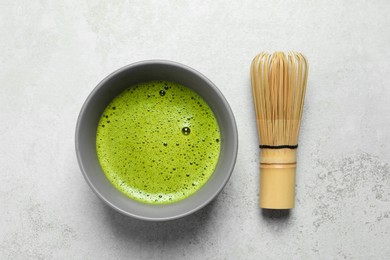 Photo of Cup of fresh green matcha tea and bamboo whisk on light grey table, flat lay