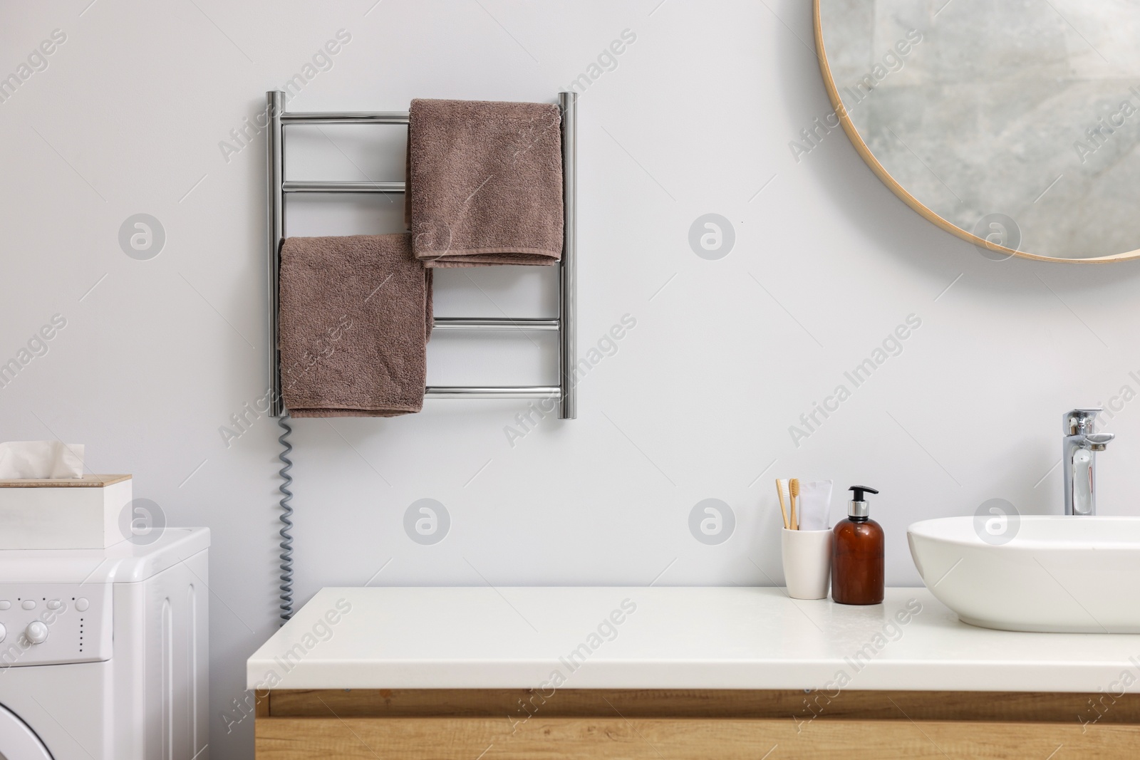 Photo of Heated towel rail with brown towels in bathroom