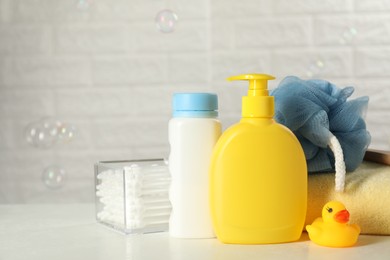 Photo of Baby cosmetic products, bath duck, cotton swabs and towel on white table against soap bubbles. Space for text
