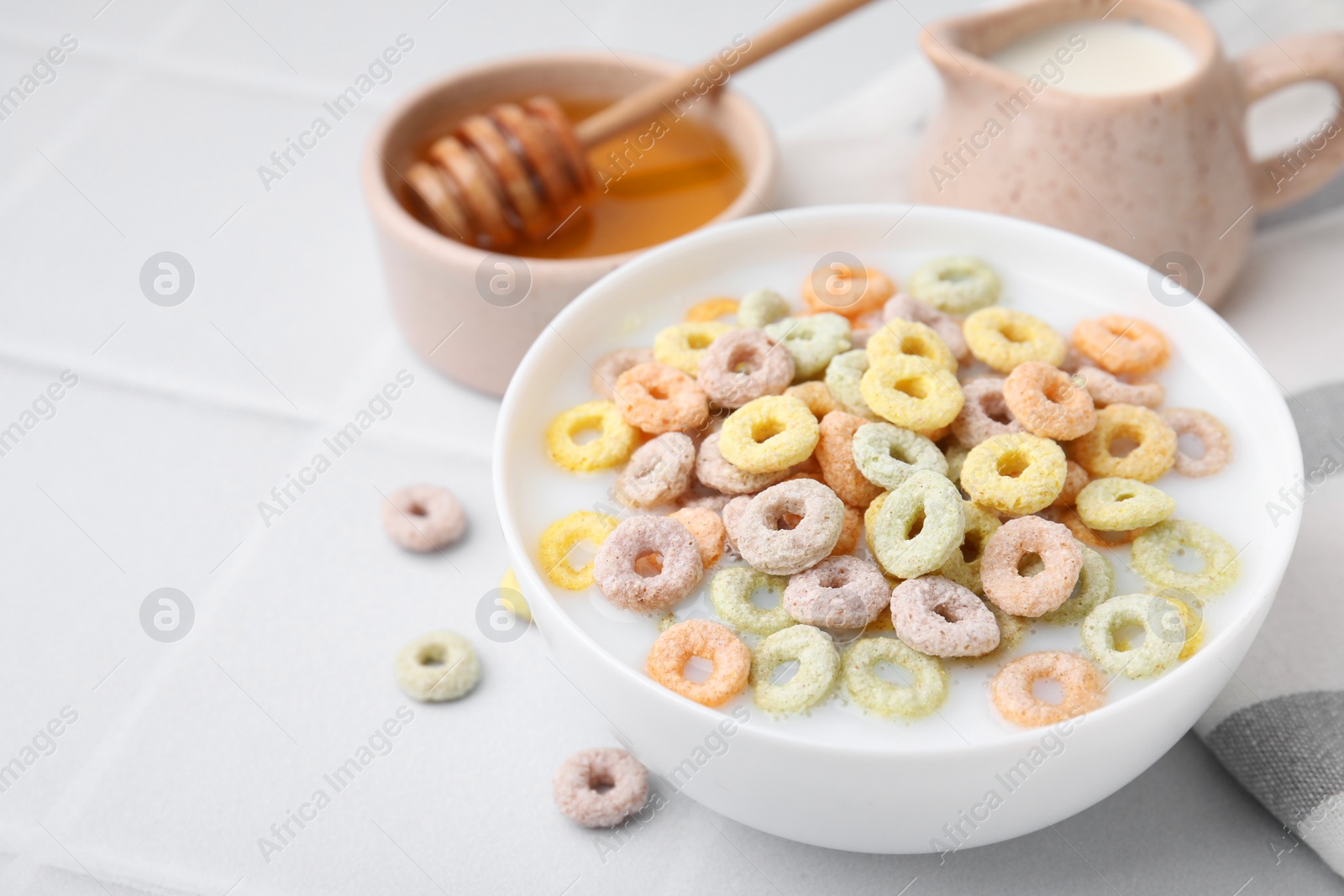 Photo of Cereal rings and milk in bowl on white tiled table, closeup. Space for text